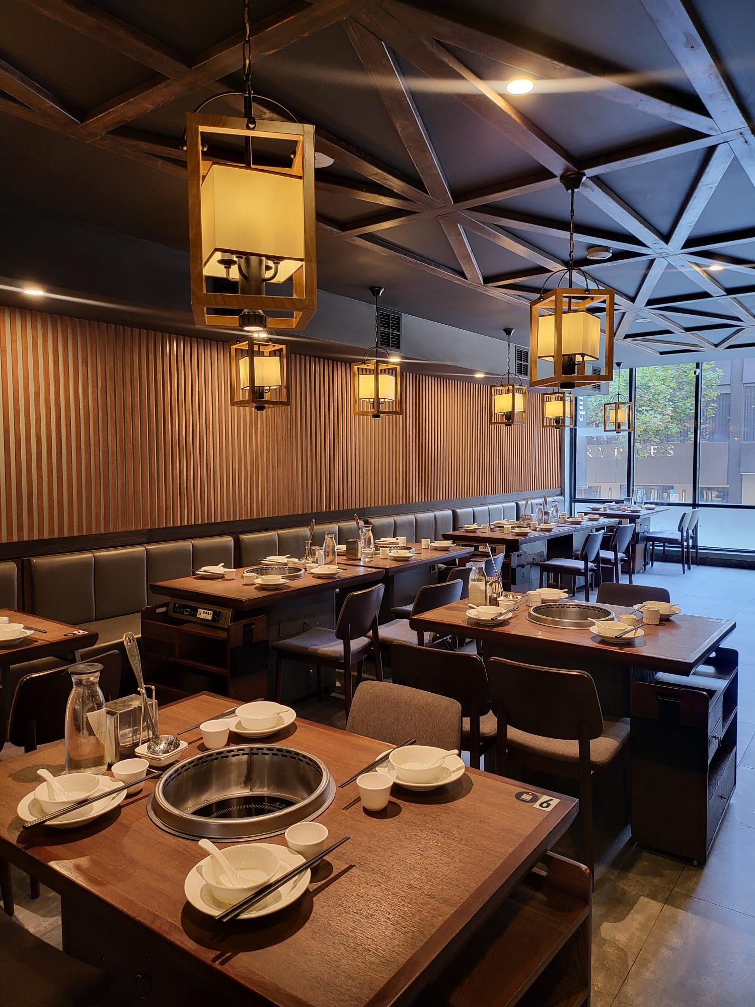 The dining room under wooden lanterns and a beamed ceiling, with a pot built into every table