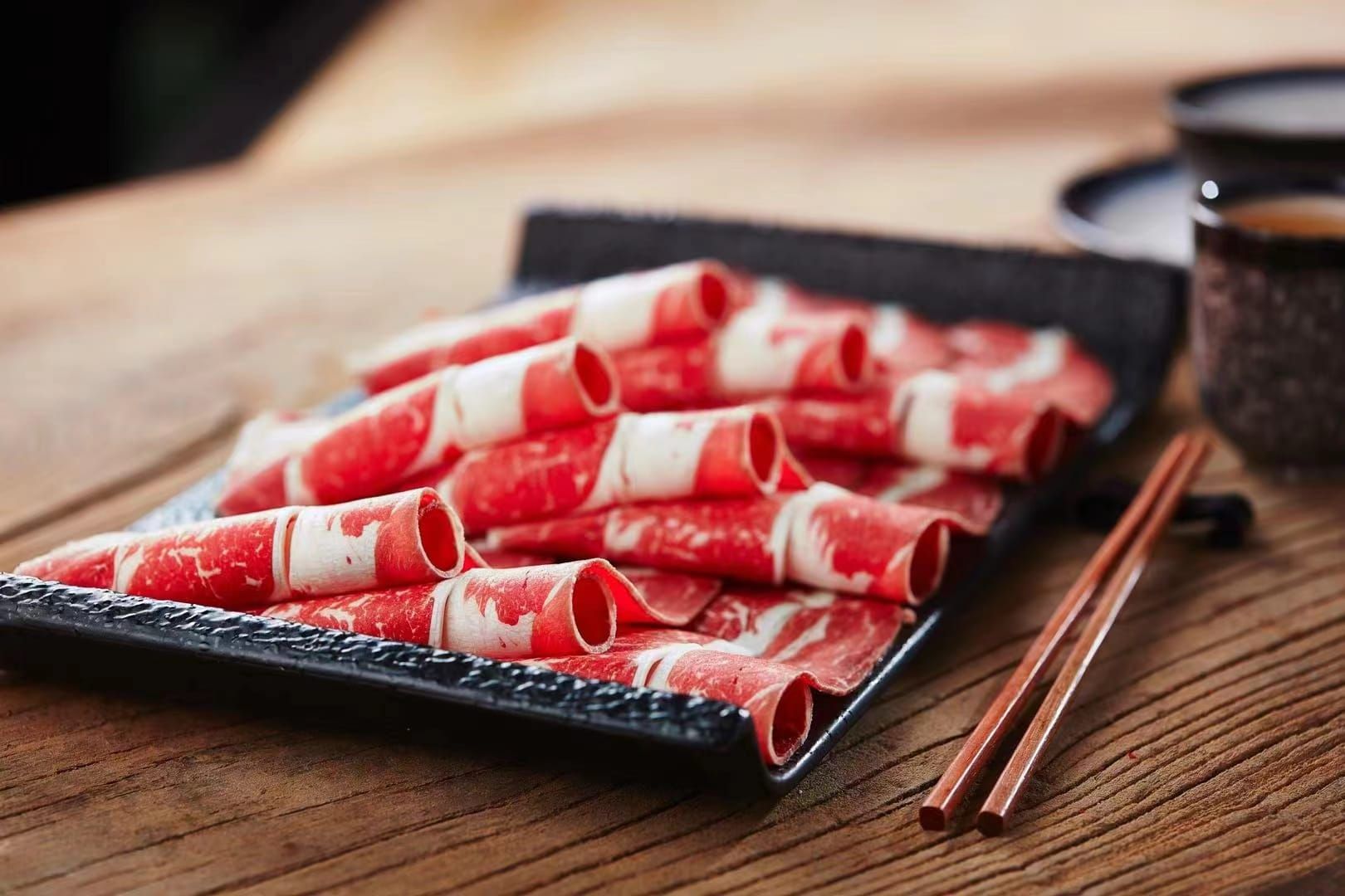 Thin rolls of sliced meat on a black stone plate, ready for the hot pot