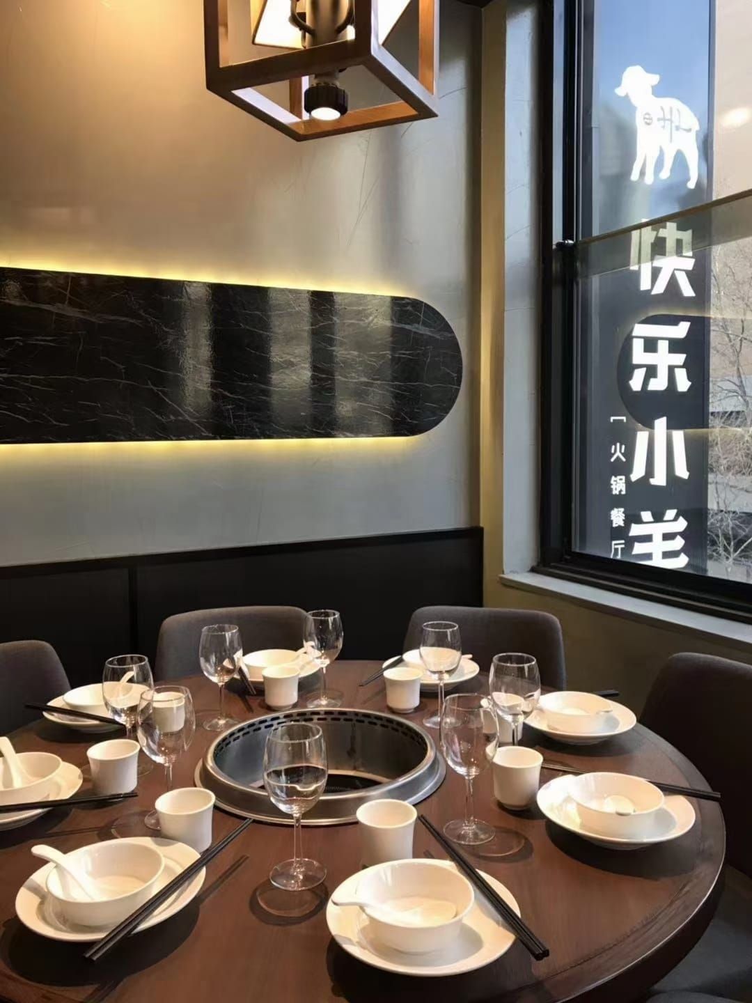 A round table set for a group by the window, with Happy Lamb’s lamb and Chinese name on the glass