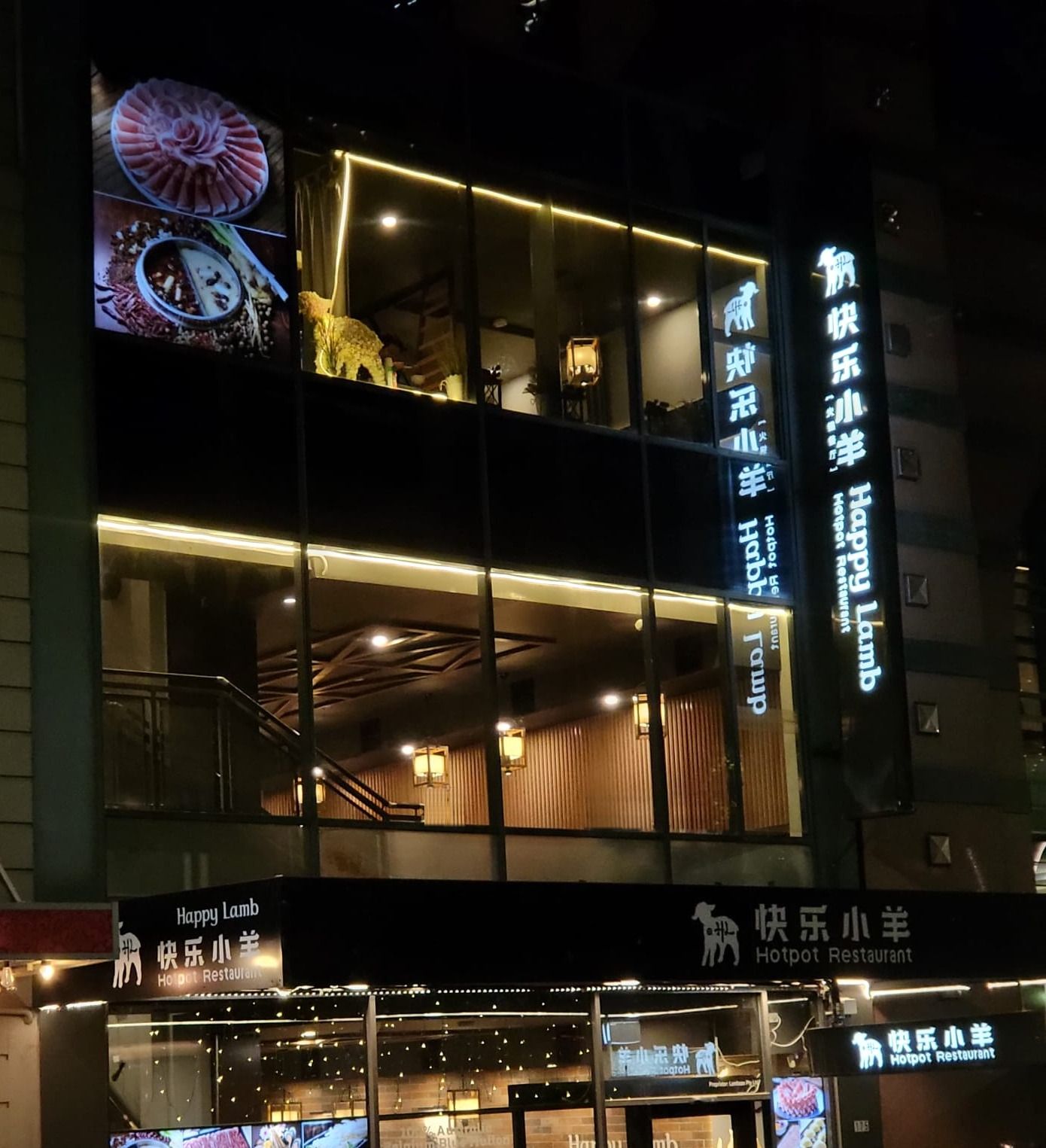 Happy Lamb Hot Pot Restaurant at night on Exhibition Street: two lit floors of dining room under the Happy Lamb and 快乐小羊 signs